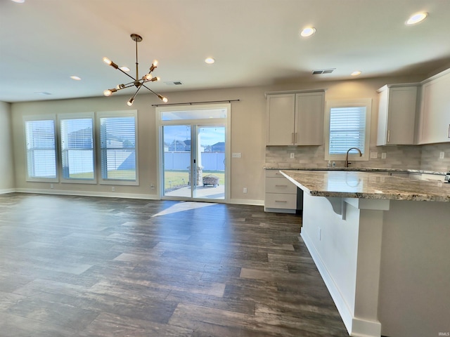 kitchen featuring hanging light fixtures, dark hardwood / wood-style flooring, backsplash, light stone countertops, and an inviting chandelier