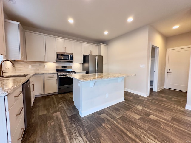 kitchen with stainless steel appliances, a center island, dark wood-type flooring, sink, and light stone counters