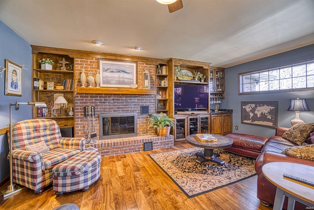 living room featuring built in features, ceiling fan, a brick fireplace, and hardwood / wood-style floors