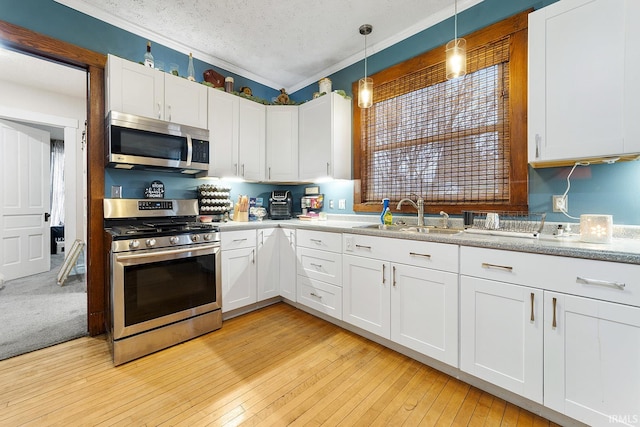 kitchen with decorative light fixtures, appliances with stainless steel finishes, light carpet, white cabinets, and sink