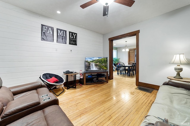 living room with wood walls, light hardwood / wood-style floors, and ceiling fan