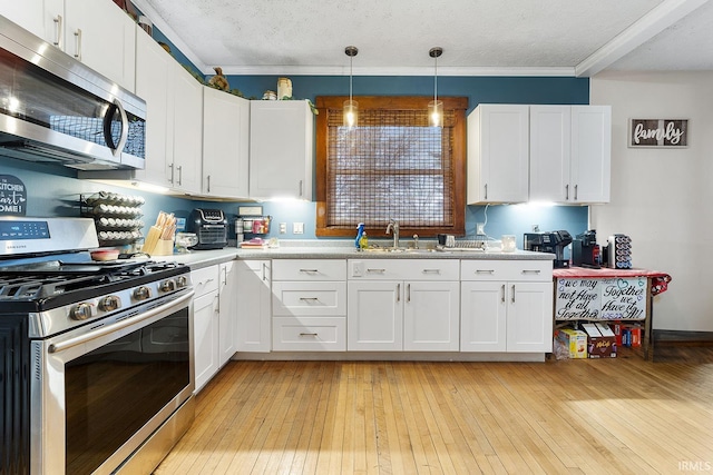 kitchen featuring appliances with stainless steel finishes, pendant lighting, light wood-type flooring, and white cabinetry