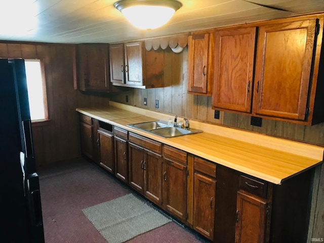 kitchen with sink, dark colored carpet, black refrigerator, and wood walls