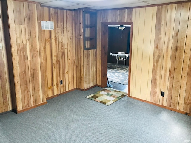 empty room with dark carpet, a paneled ceiling, and wood walls