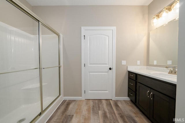 full bathroom with a stall shower, vanity, baseboards, and wood finished floors