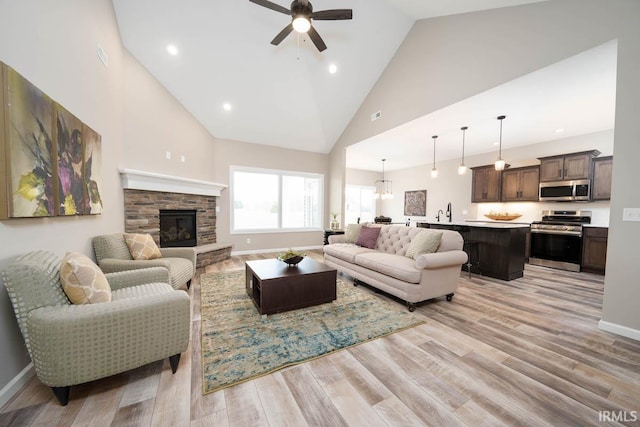 living room featuring a stone fireplace, a ceiling fan, light wood-type flooring, and high vaulted ceiling