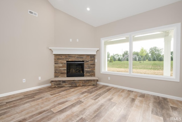 unfurnished living room with wood finished floors, baseboards, visible vents, a stone fireplace, and vaulted ceiling