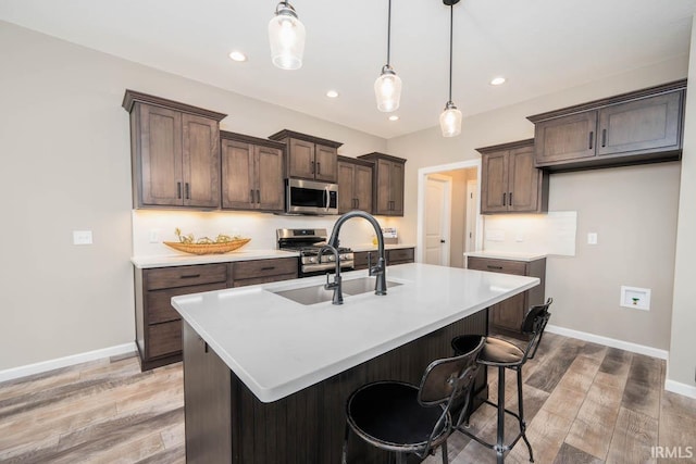 kitchen featuring light wood finished floors, a kitchen island with sink, a sink, light countertops, and appliances with stainless steel finishes