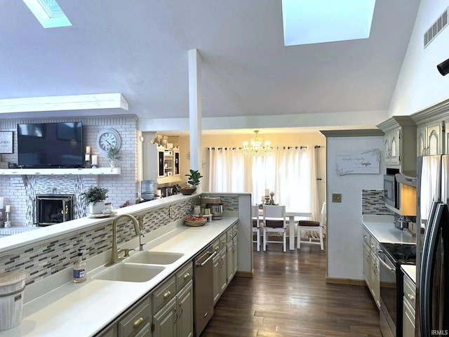 kitchen featuring stainless steel appliances, a brick fireplace, a chandelier, lofted ceiling with skylight, and dark hardwood / wood-style floors