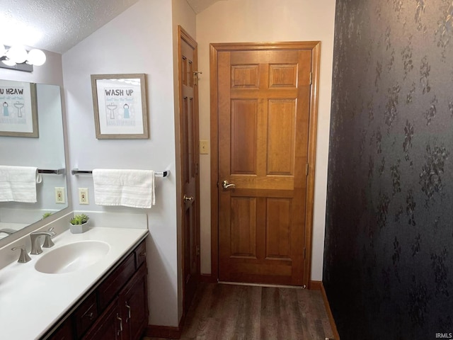 bathroom featuring wood-type flooring, a textured ceiling, vanity with extensive cabinet space, and vaulted ceiling