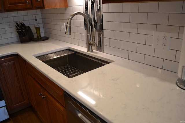 kitchen with backsplash, sink, dishwasher, and light stone counters