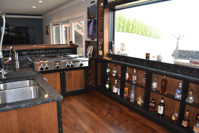 kitchen with dark hardwood / wood-style floors, stainless steel gas stovetop, ornamental molding, dark stone countertops, and sink