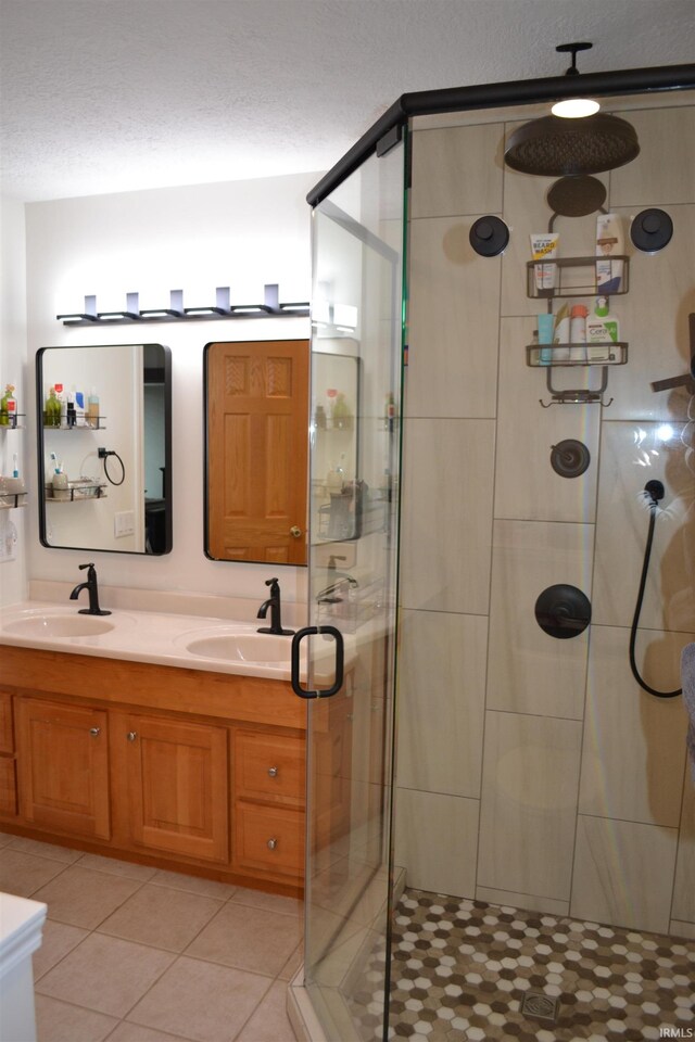 bathroom featuring double sink, tile flooring, a textured ceiling, vanity with extensive cabinet space, and a shower with shower door