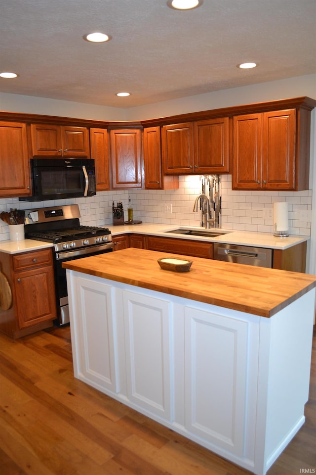 kitchen with wooden counters, tasteful backsplash, light hardwood / wood-style flooring, appliances with stainless steel finishes, and sink