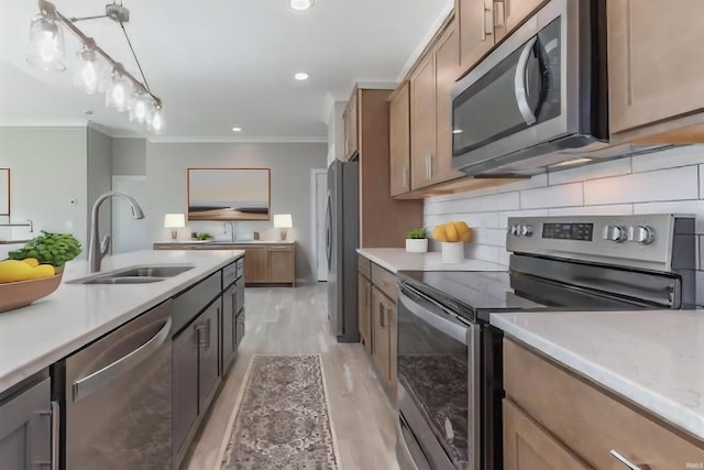 kitchen with appliances with stainless steel finishes, light wood-type flooring, sink, crown molding, and decorative light fixtures