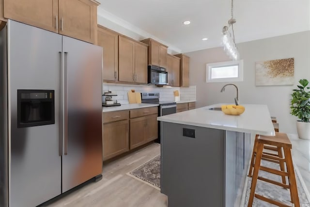 kitchen featuring hanging light fixtures, an island with sink, appliances with stainless steel finishes, light hardwood / wood-style flooring, and sink