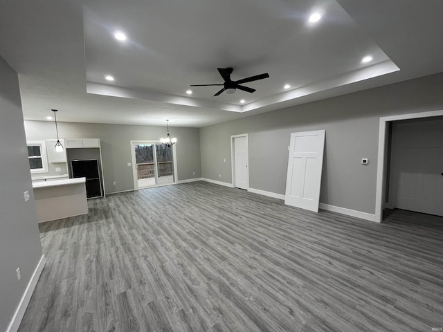 unfurnished living room with a raised ceiling, ceiling fan with notable chandelier, and hardwood / wood-style floors