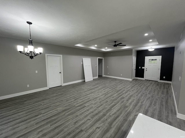 unfurnished living room featuring a raised ceiling, dark hardwood / wood-style floors, and ceiling fan with notable chandelier