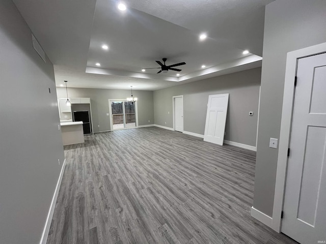 unfurnished living room featuring ceiling fan with notable chandelier, hardwood / wood-style floors, and a tray ceiling