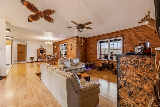 living room with light hardwood / wood-style floors, ceiling fan with notable chandelier, wood walls, and vaulted ceiling