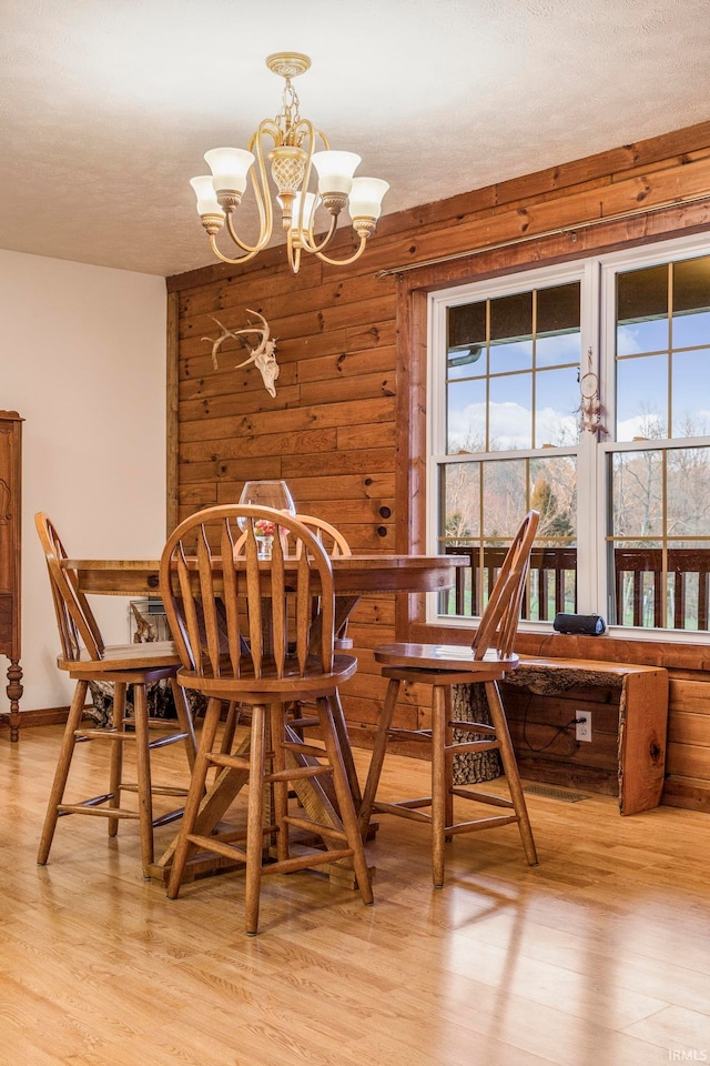 dining space featuring plenty of natural light, a notable chandelier, wood walls, and light wood-type flooring