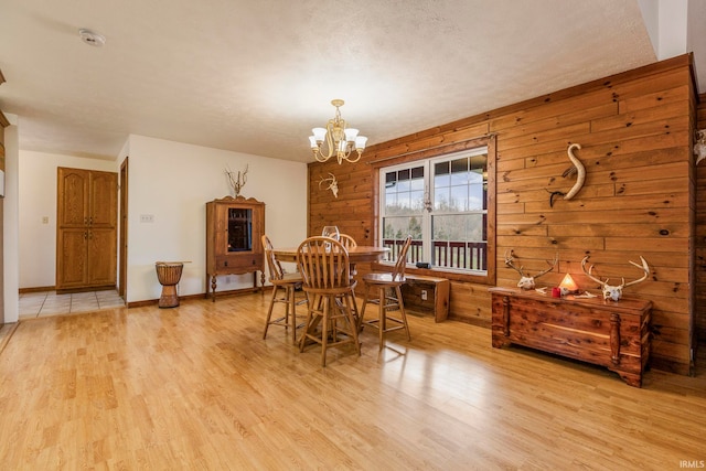 dining room with a notable chandelier, wood walls, and light hardwood / wood-style floors