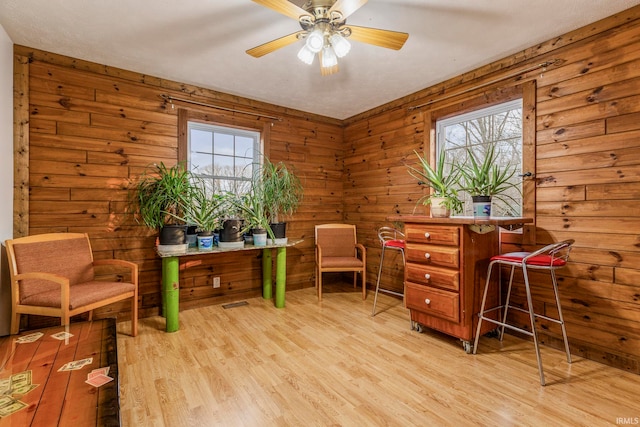 interior space with ceiling fan, wood walls, light wood-type flooring, and plenty of natural light