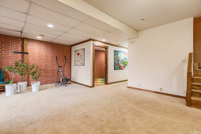 interior space with a paneled ceiling, light carpet, and brick wall