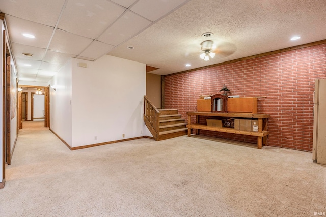 basement featuring a paneled ceiling, brick wall, ceiling fan, and light colored carpet