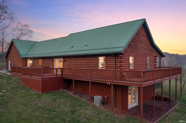 back house at dusk featuring a lawn, central air condition unit, and a wooden deck