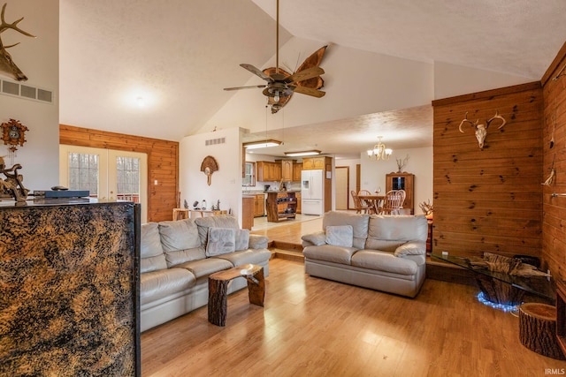 living room with wooden walls, light hardwood / wood-style flooring, high vaulted ceiling, and ceiling fan with notable chandelier