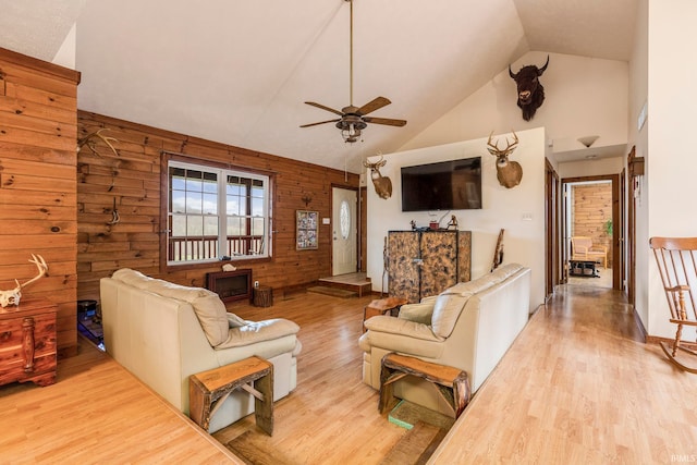 living room with ceiling fan, high vaulted ceiling, light hardwood / wood-style floors, and wooden walls