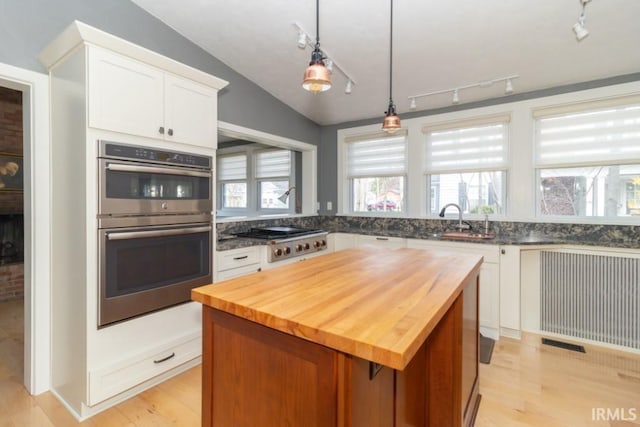 kitchen with a kitchen island, rail lighting, appliances with stainless steel finishes, wood counters, and white cabinetry