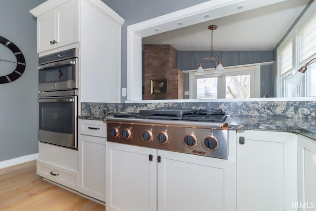 kitchen with appliances with stainless steel finishes, dark stone countertops, vaulted ceiling, light hardwood / wood-style floors, and white cabinetry