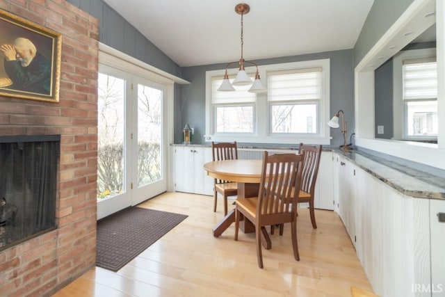 dining space featuring a fireplace, brick wall, light wood-type flooring, and plenty of natural light