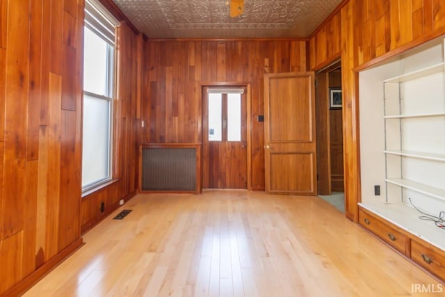 empty room featuring radiator, wood walls, light hardwood / wood-style flooring, and a wealth of natural light