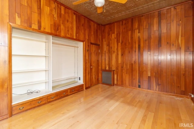 empty room with wood walls, ceiling fan, and light hardwood / wood-style flooring