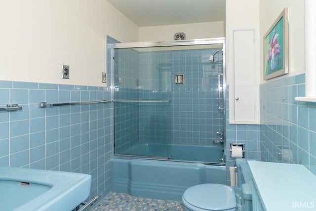 full bathroom with tile walls, tile floors, toilet, and bath / shower combo with glass door