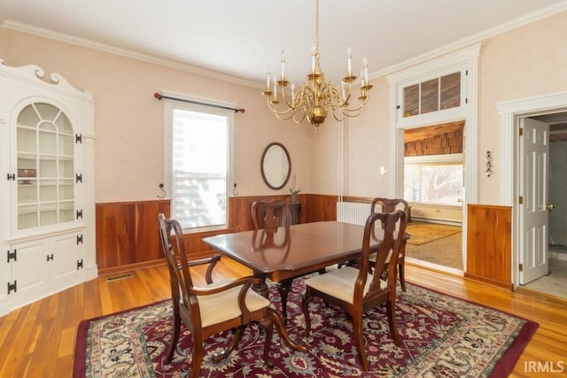 dining area with an inviting chandelier, radiator, ornamental molding, and light wood-type flooring