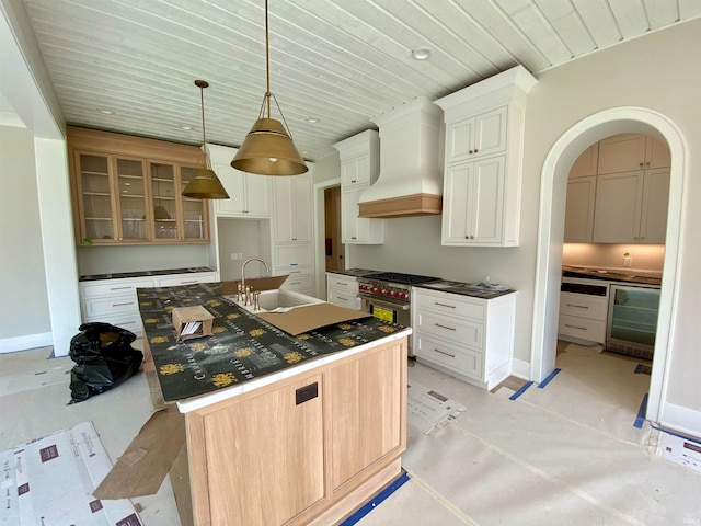 kitchen with pendant lighting, premium range hood, range with two ovens, a kitchen island with sink, and sink