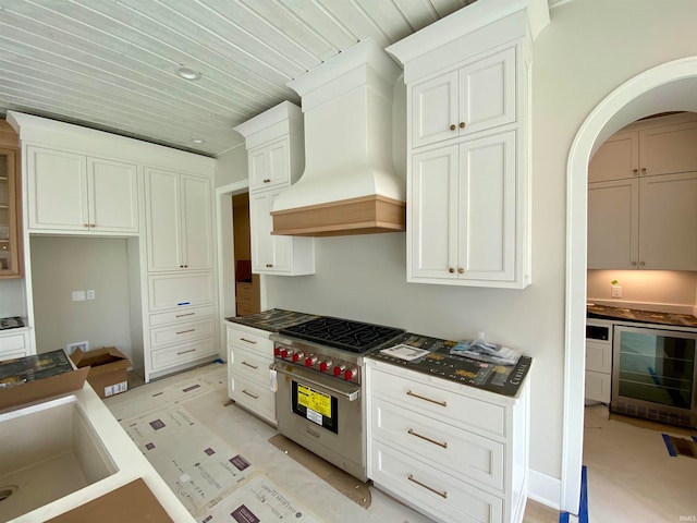 kitchen featuring custom exhaust hood, wine cooler, white cabinets, designer range, and sink