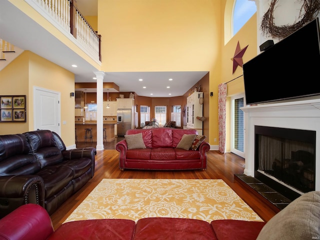 living room with dark hardwood / wood-style floors, decorative columns, and a towering ceiling