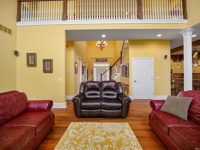 living room with dark hardwood / wood-style floors, an inviting chandelier, a towering ceiling, and ornate columns