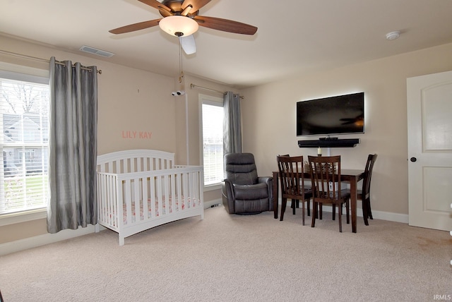 bedroom featuring ceiling fan, light carpet, and a nursery area