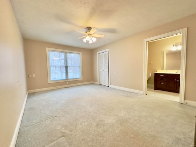 unfurnished bedroom featuring ceiling fan, a closet, connected bathroom, and light carpet