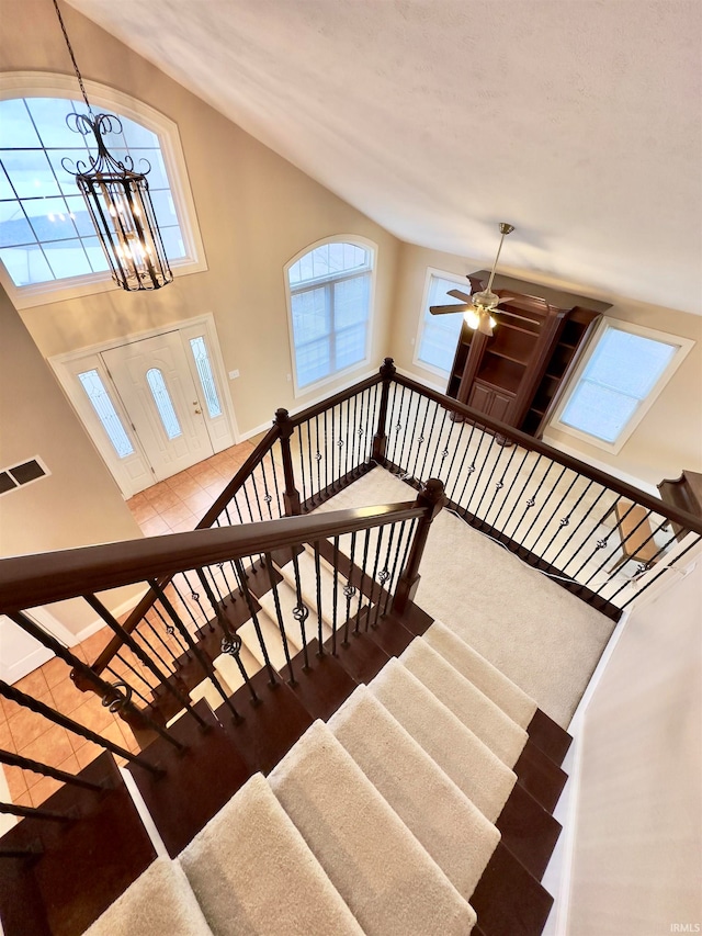 stairway featuring hardwood / wood-style flooring, plenty of natural light, a high ceiling, and ceiling fan with notable chandelier