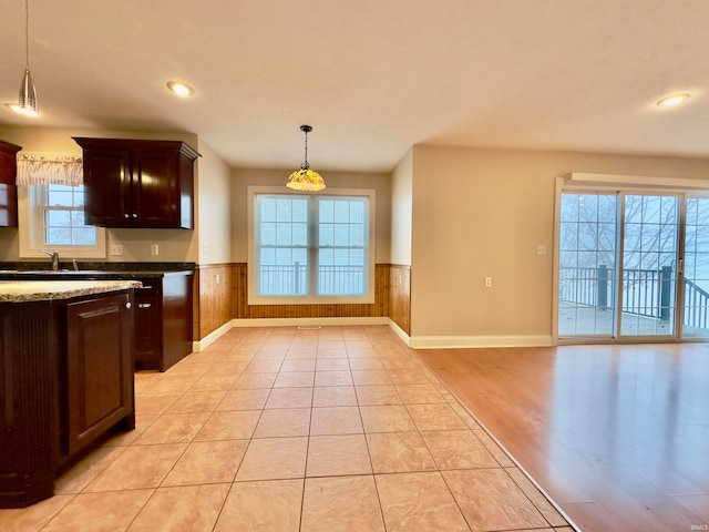 kitchen with light stone countertops, dark brown cabinets, hanging light fixtures, light wood-type flooring, and sink