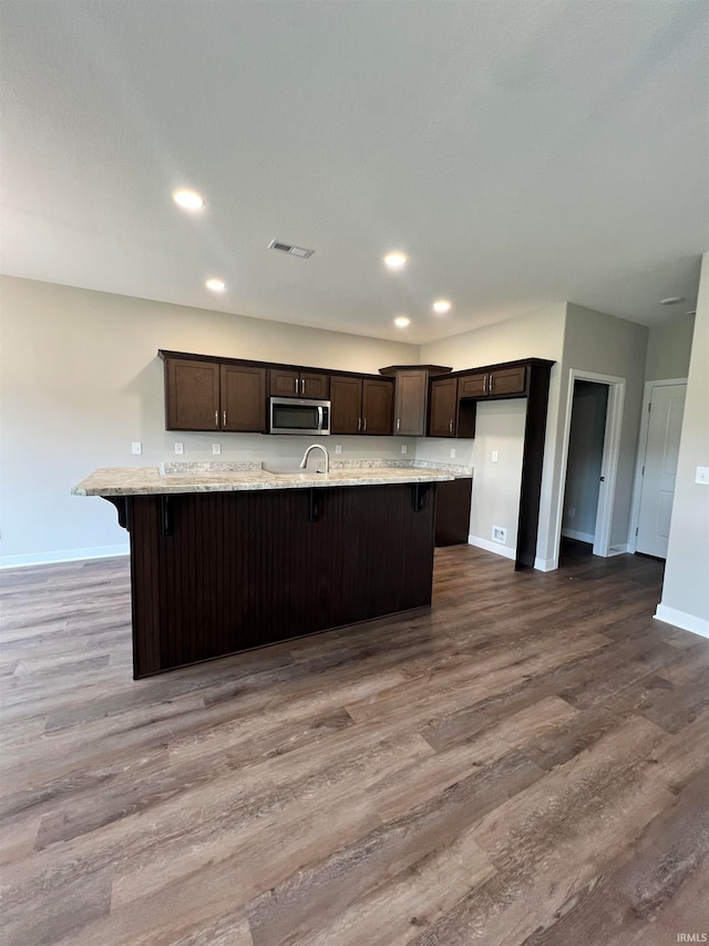 kitchen with dark brown cabinets, hardwood / wood-style floors, and an island with sink