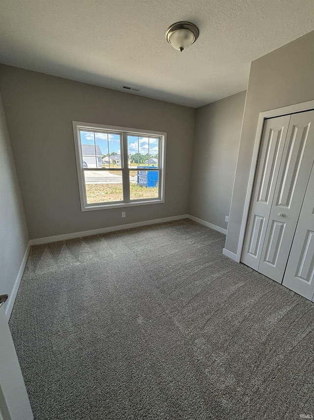 unfurnished bedroom with visible vents, a textured ceiling, a closet, carpet, and baseboards