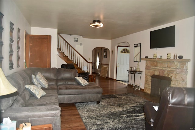 living room featuring a stone fireplace and dark wood-type flooring